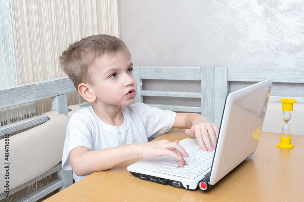 A cute little boy sits at the table and thinks how to do homework. The boy is watching a video tutorial on a laptop. Learning concept, distance learning, video conferencing lesson with mentor A cute little boy sits at the table and thinks how to do homework. The boy is watching a video tutorial on a laptop. Learning concept, distance learning, video conferencing lesson with mentor