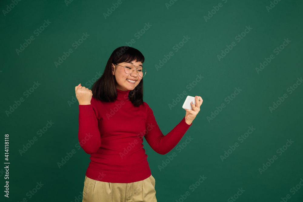 Winner, videogame, cheerful. East asian young beautiful woman's portrait on green background with copyspace. Brunette model. Concept of human emotions, facial expression, sales, ad, fashion.