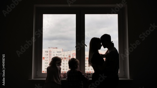 Silhouette of lovers with children on the background of windows from a new apartment.