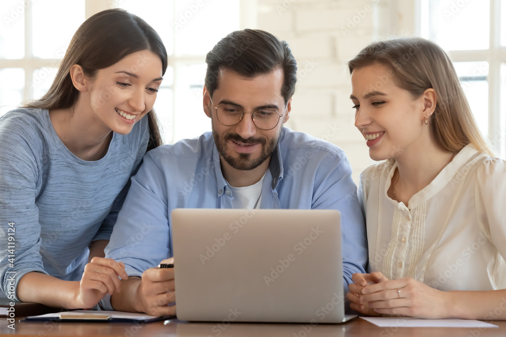 Smiling young male manager looking at computer screen with happy two female colleagues, discussing online project development, working brainstorming in office, using software or enjoying break time. Smiling young male manager looking at computer screen with happy two female colleagues, discussing online project development, working brainstorming in office, using software or enjoying break time.