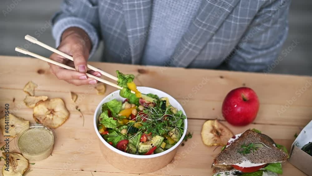 Woman wearing silver suite eating vegan food with chop sticks at the office