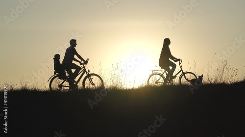 Friendly family with a child on bicycles during sunset.