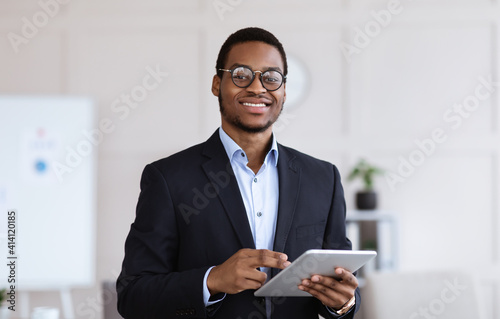 Cheerful black man manager holding digital tablet, office interior photo