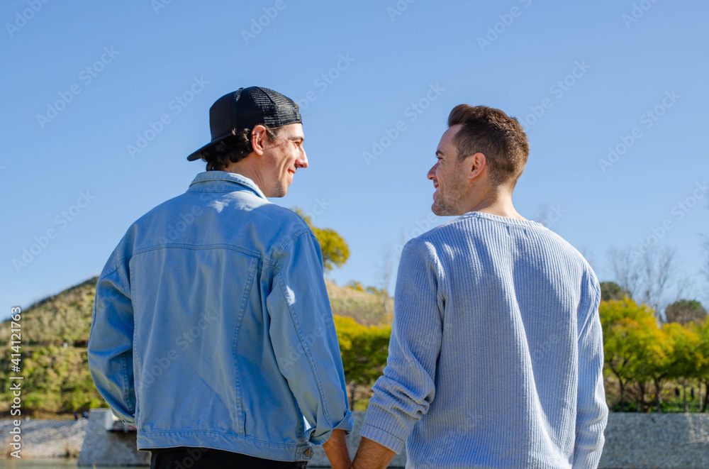 Casual Young Gay Couple Smiling Looking at each other While Holding Their Hands at the Park in Spring Casual Young Gay Couple Smiling Looking at each other While Holding Their Hands at the Park in Spring