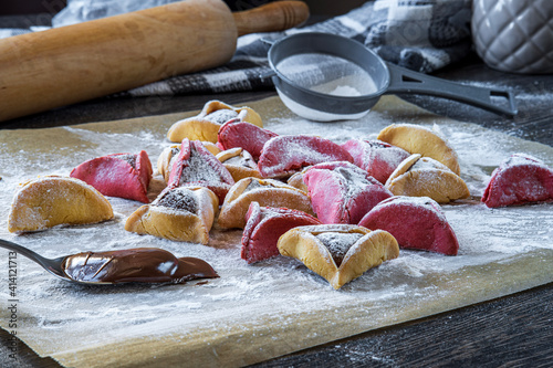 Colorful hamantaschen cookies with sugar powder in a kitchen. Jewish traditional pastry for Purim (Jewish carnival holiday with celebration concept). Homemade gluten free cookie filled with chocolate photo