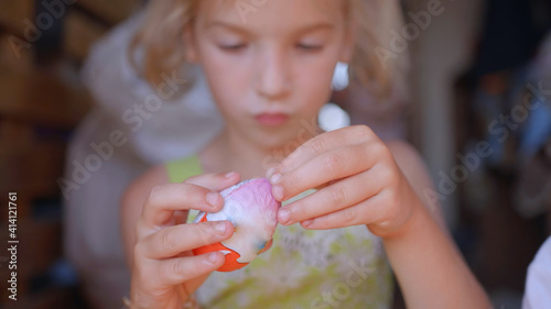 A little girl unfolds and eats a chocolate egg with toys.