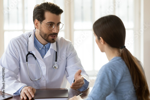 Картината върху платно Pleasant young handsome male doctor in white uniform giving professional surgeon consultation to woman patient, explaining disease treatment protocol or discussing health condition at meeting