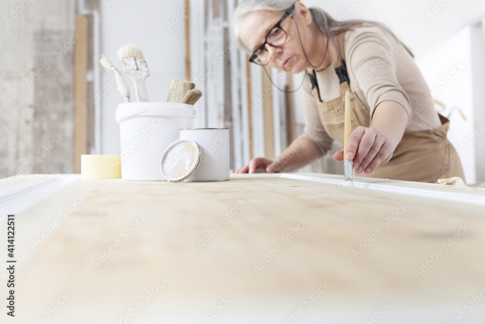 wood crafts, woman artisan carpenter painting with brush and paint jar white the door in workshop, wearing overall and eyeglasses, interior designer, restoration, diy and handmade works concept wood crafts, woman artisan carpenter painting with brush and paint jar white the door in workshop, wearing overall and eyeglasses, interior designer, restoration, diy and handmade works concept