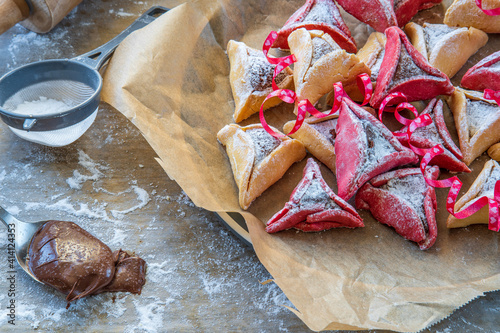 Colorful hamantaschen cookies with sugar powder on a baking sheet. Jewish traditional pastry for Purim (Jewish carnival holiday with celebration concept). Homemade gluten free cookie, chocolate filled photo