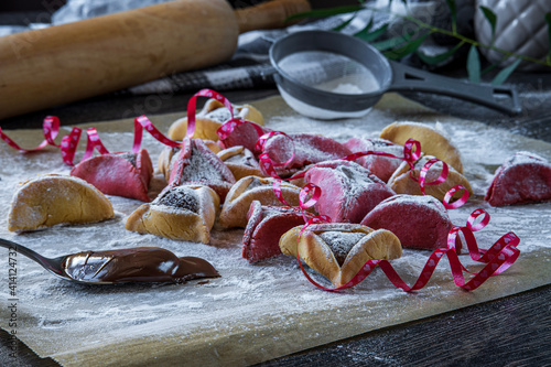 Colorful hamantaschen cookies with sugar powder in a kitchen. Jewish traditional pastry for Purim (Jewish carnival holiday with celebration concept). Homemade gluten free cookie filled with chocolate