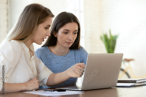 Quadro em tela Focused young female leader helping newbie colleague with software applications, working on computer in office