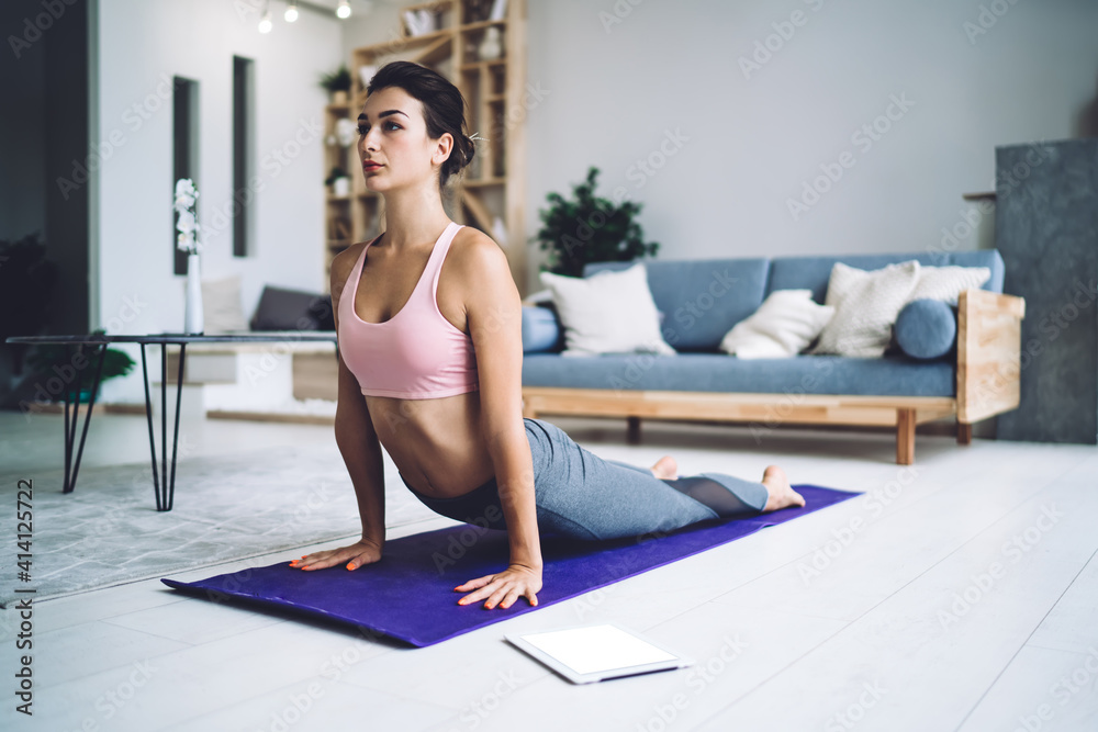 Focused young sportswoman practicing yoga at home