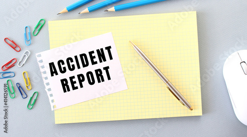ACCIDENT REPORT is written on a piece of paper that lies on a notebook next to office supplies.