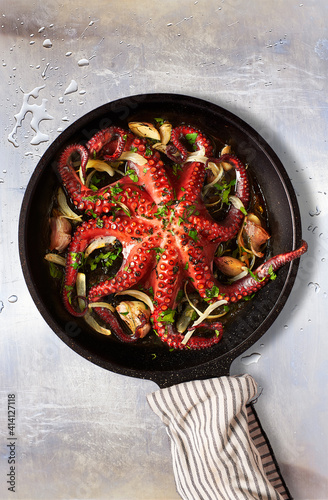 Octopus Lagareiro style dressed with onion and garlics cloves on an aged metallic table. Portuguese cuisine. photo