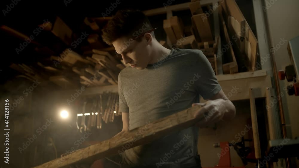 Young carpenter checks the quality of wood for making a beautiful piece of furniture and looking at it with love in his workshop. Young carpenter checks the quality of wood for making a beautiful piece of furniture and looking at it with love in his workshop.