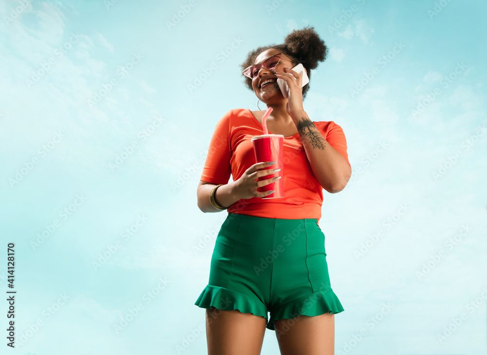 Phone talks. Portrait of young female fashion model on blue sky background. Beautiful african woman with trendy make-up and bright appearance. Style and beauty concept, summer mood. Copyspace for ad. Phone talks. Portrait of young female fashion model on blue sky background. Beautiful african woman with trendy make-up and bright appearance. Style and beauty concept, summer mood. Copyspace for ad.