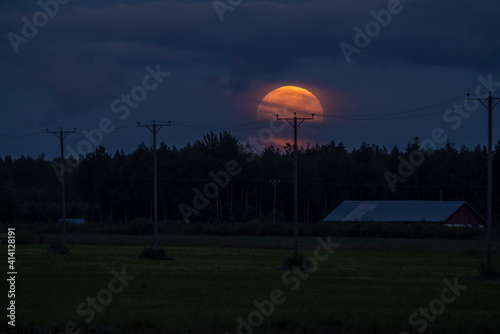 full buck moon in a farm field with barn and power lines