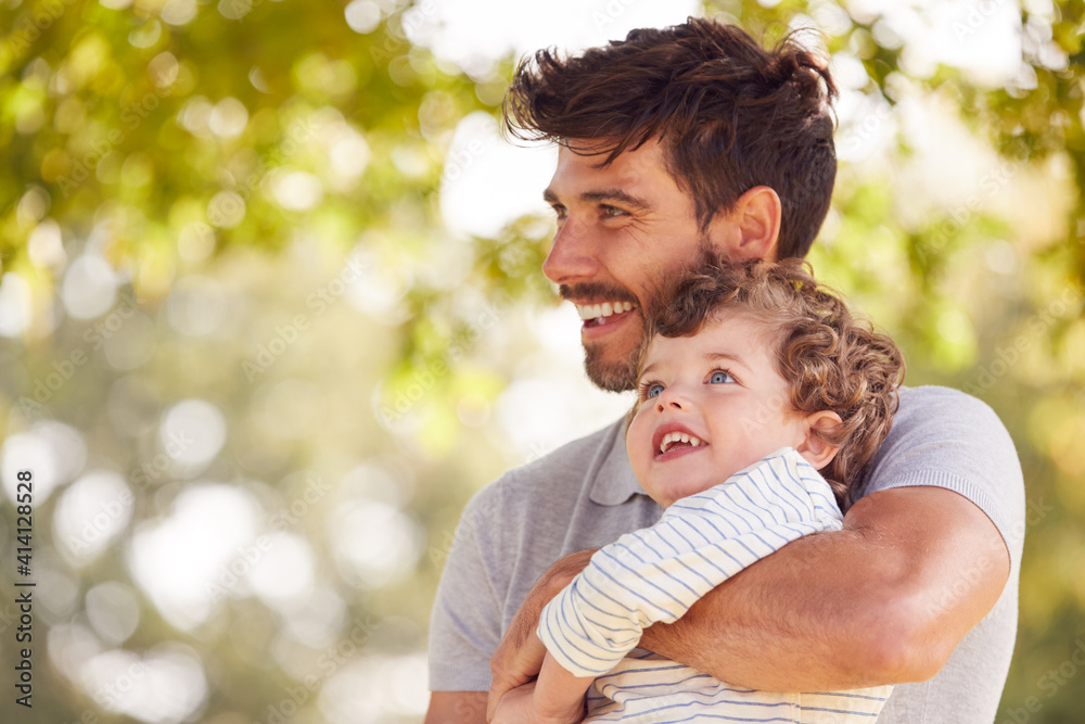 Fototapeta premium Loving Father With Son Having Fun In Park Holding Him In The Air Against Leafy Background