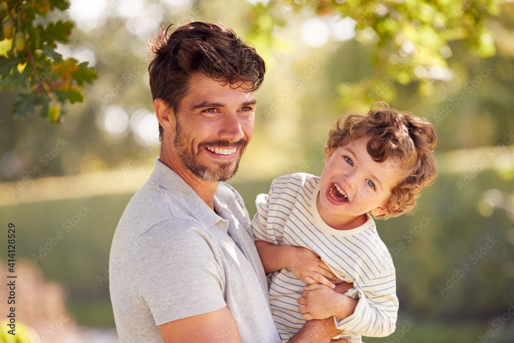 Loving Father With Son Having Fun In Park Holding Him In The Air Against Leafy Background Loving Father With Son Having Fun In Park Holding Him In The Air Against Leafy Background