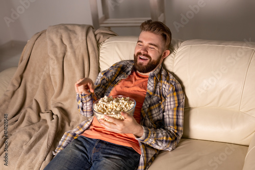 Bearded man watching film or sport games TV eating popcorn in house at night. Cinema, championship and fan concept.