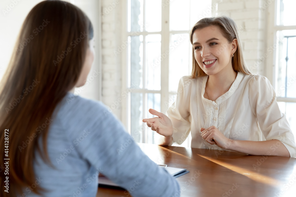 Smiling confident beautiful young woman involved in conversation with hr manager at meeting. Happy millennial female job seeker making self-presentation to employer, good first impression concept. Smiling confident beautiful young woman involved in conversation with hr manager at meeting. Happy millennial female job seeker making self-presentation to employer, good first impression concept.