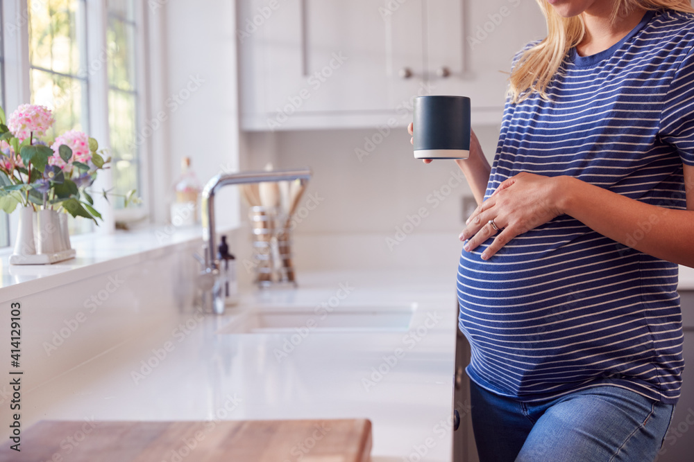Close Up Of Pregnant Woman Standing By Kitchen Window Touching Stomach Relaxing With Hot Drink Close Up Of Pregnant Woman Standing By Kitchen Window Touching Stomach Relaxing With Hot Drink