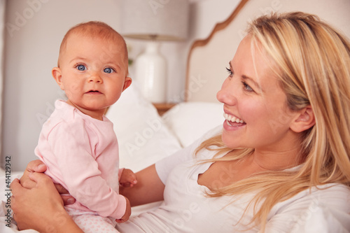 Loving Mother In Bed Playing Game With Baby Daughter Wearing Pyjamas