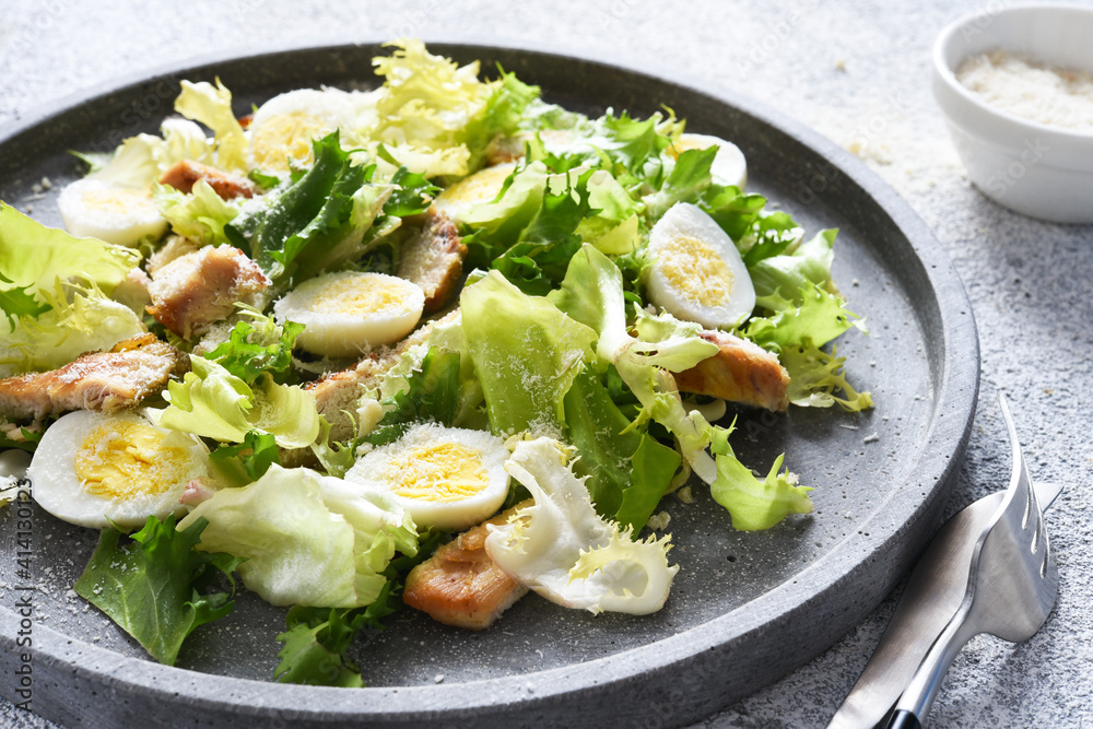Traditional caesar salad with grilled chicken and parmesan on a concrete plate. Traditional caesar salad with grilled chicken and parmesan on a concrete plate.
