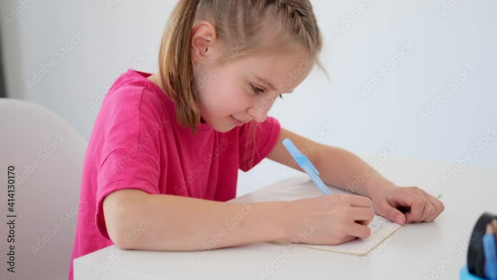 Schoolgirl writing in textbook with pen during lesson at school Schoolgirl writing in textbook with pen during lesson at school