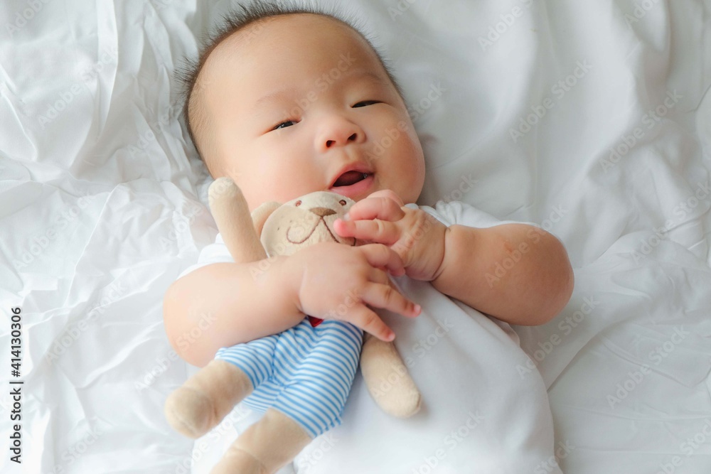 Cute asian newborn toddler with a toy on white bed at home. Cute asian newborn toddler with a toy on white bed at home.