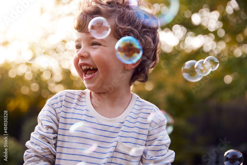 Young Boy Having Fun In Garden Chasing And Bursting Bubbles