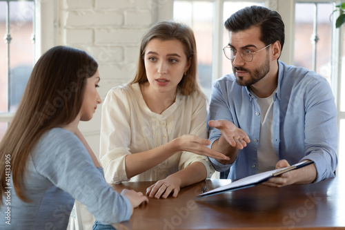 Unhappy young family couple clients feeling stressed with bad contract offer, showing dissatisfaction to broker or dealer. Angry millennial spouses arguing with real estate agent at office meeting.