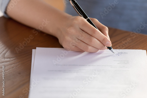 Close up focus on female hand putting signature at paper contract document. Young woman signing medical insurance agreement after making choice of family doctor or general practitioner in hospital.