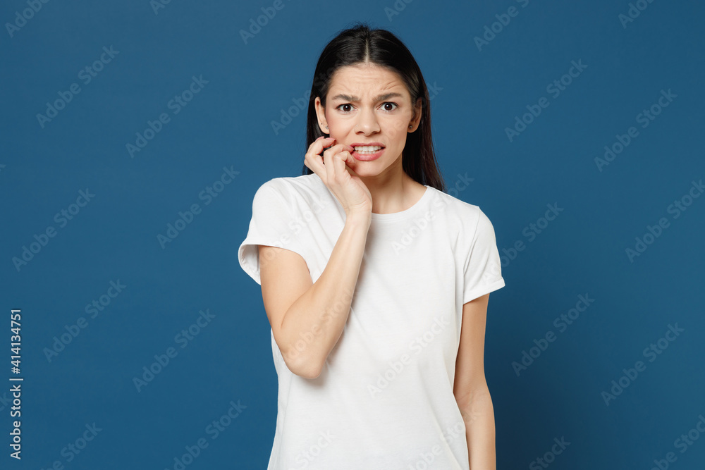 Young troubled thoughtful pensive worrying scared mistaken latin woman 20s wearing white casual basic t-shirt biting nails fingers look camera isolated on dark blue color background studio portrait. Young troubled thoughtful pensive worrying scared mistaken latin woman 20s wearing white casual basic t-shirt biting nails fingers look camera isolated on dark blue color background studio portrait.