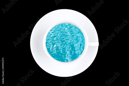 White cup with sea or ocean turquoise water isolated on black background. Sea or ocean waves in cup. Abstract top view ocean or sea in cup