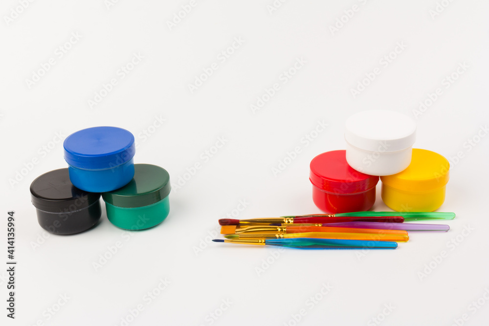 Closed plastic jars with paint of different colors for children's creativity on white background. Paint bottles with paint brushes for art Closed plastic jars with paint of different colors for children's creativity on white background. Paint bottles with paint brushes for art