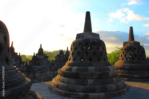 Borobudur temple in Jogjakarta Indonesia. Central Java. Picture of the temple Borobudur at sunset with blue sky and green trees. Multiple stupa s shown in foreground of photo. Stupa s at sunset. 