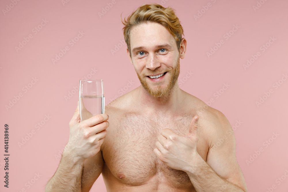 Smiling bearded naked young man 20s perfect skin hold drinking clear fresh pure water from glass showing thumb up isolated on pink background studio. Skin care healthcare cosmetic procedures concept. Smiling bearded naked young man 20s perfect skin hold drinking clear fresh pure water from glass showing thumb up isolated on pink background studio. Skin care healthcare cosmetic procedures concept.