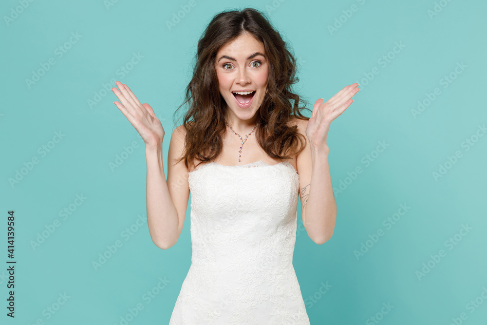 Surprised tender bride young woman 20s in beautiful white wedding dress spreading hands keeping mouth open isolated on blue turquoise background studio portrait. Ceremony celebration party concept. Surprised tender bride young woman 20s in beautiful white wedding dress spreading hands keeping mouth open isolated on blue turquoise background studio portrait. Ceremony celebration party concept.
