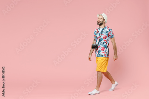 Full length side view cheerful young traveler tourist man in summer clothes hat walking going isolated on pink background studio portrait. Passenger traveling on weekends. Air flight journey concept.