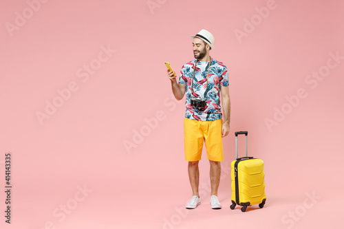 Full length of smiling young traveler tourist man using mobile phone booking hotel taxi isolated on pink color background studio portrait. Passenger traveling on weekends. Air flight journey concept.