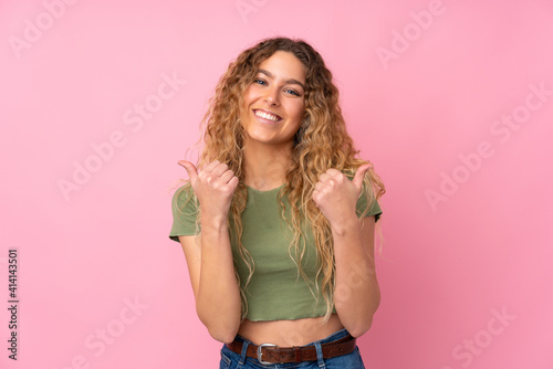 Young blonde woman with curly hair isolated on pink background with thumbs up gesture and smiling