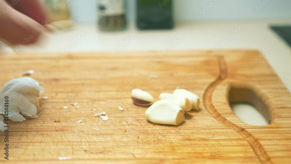 close-up of male hands chopping garlic on a wooden cutting board.