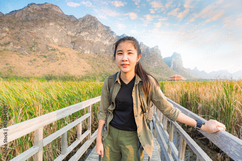 Naklejka premium Freedom traveler woman standing with raised arms and enjoying a beautiful nature and cheering young woman backpacker at sunrise seaside mountain peak