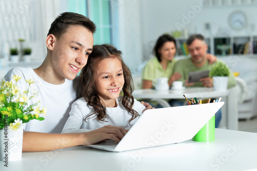 brother and sister using laptop while sitting at table
