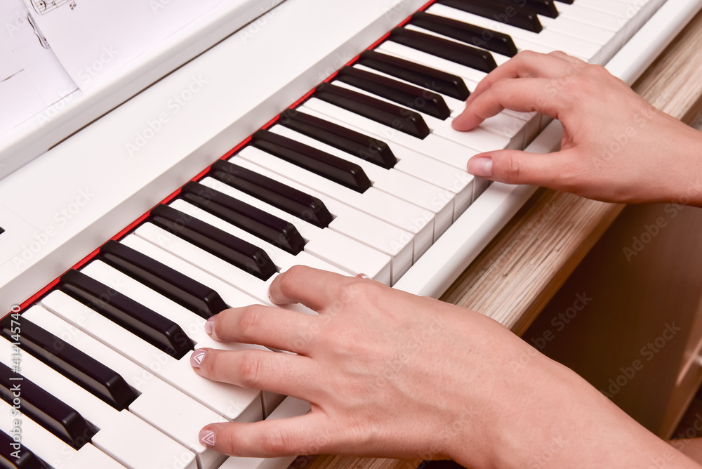 Obraz premium Woman's hands playing electronic digital piano at home. The woman is professional pianist arranging music using piano electronic keyboards. Musician practicing keyboard composing music