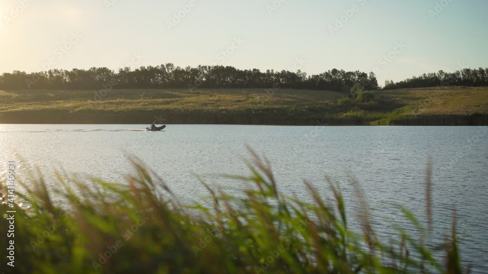 A man rides a motor boat in an inflatable boat on a lake at sunset. Fisherman rides a motor boat on the river.