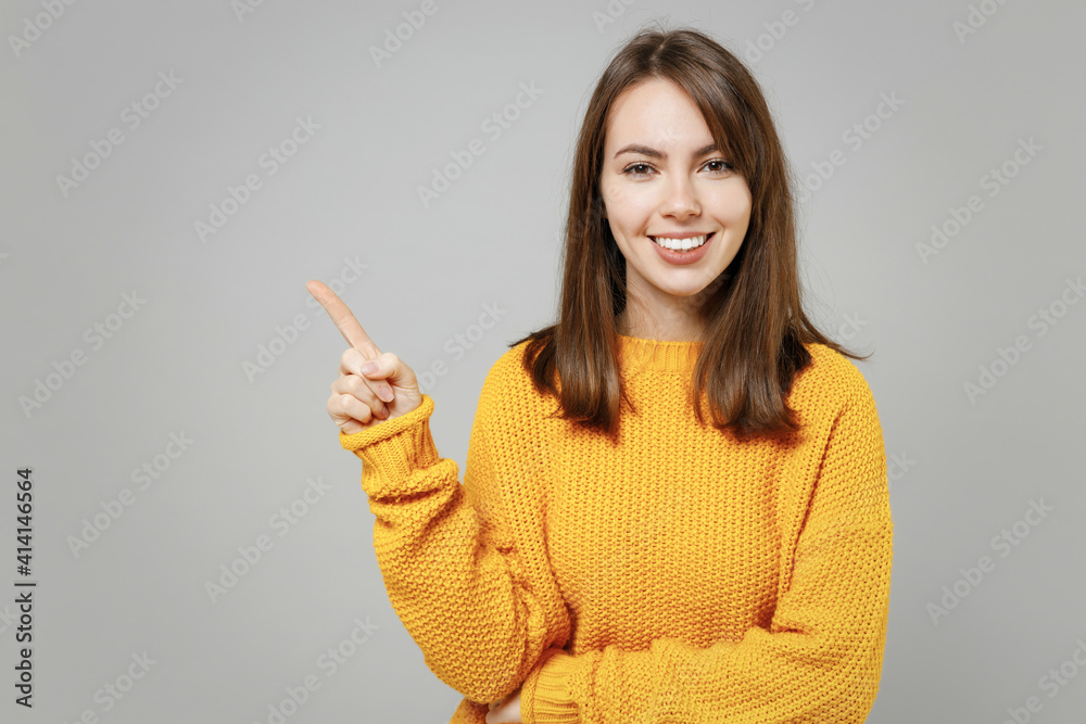 Young excited happy smiling friendly cheerful caucasian woman in casual knitted yellow sweater point index finger aside on copy space area mock up isolated on grey color background studio portrait Young excited happy smiling friendly cheerful caucasian woman in casual knitted yellow sweater point index finger aside on copy space area mock up isolated on grey color background studio portrait