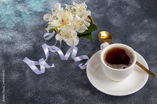 White cup with coffee on a gray background. A bouquet of orchids entwined with a ribbon in the background. Banners, congratulations on the holiday.