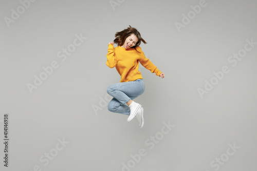 Full length of young excited overjoyed happy lucky positive attractive woman 20s wearing knitted yellow sweater do winner gesture clench fist jumping high isolated on grey background studio portrait Fototapet